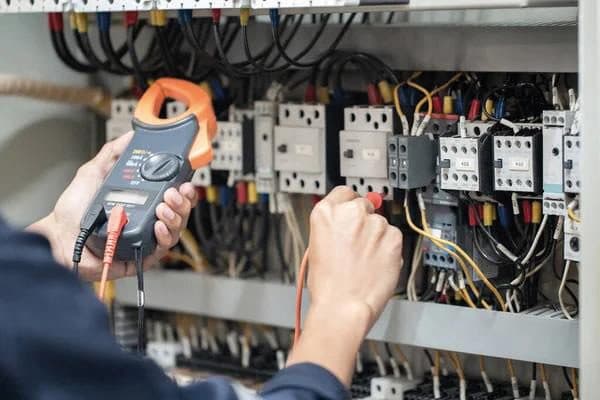 Technician testing a control panel with a clamp meter